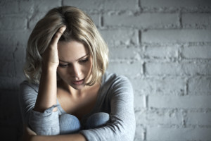 A pretty young blonde woman sitting down while looking severely depressed